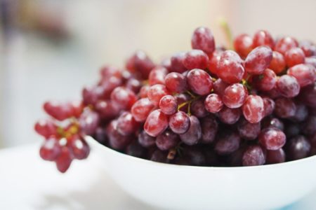 Foto colorida de pote branco com uvas roxas - Metrópoles