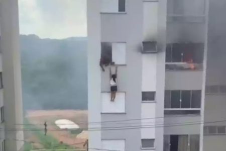 Foto colorida de mulher pendurada em janela de prédio depois de criança colocar fogo na casa dos avós - Metrópoles