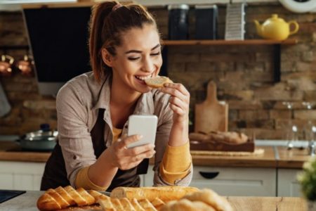 Mulher comendo pão com um café debruçada a mesa - Metrópoles
