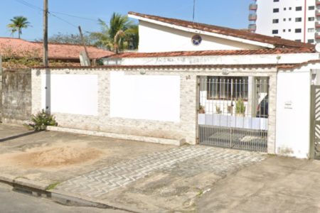 Foto colorida mostra fachada de casa com muro branco em dia de sol