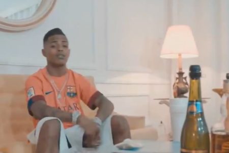 Imagem colorida mostra o rapper LK Metralha, um homem negro, vestido com uma camisa do Barcelona na cor salmão - Metrópoles