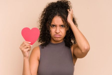 Mulher segurando um coração de papel nas mãos com cara triste