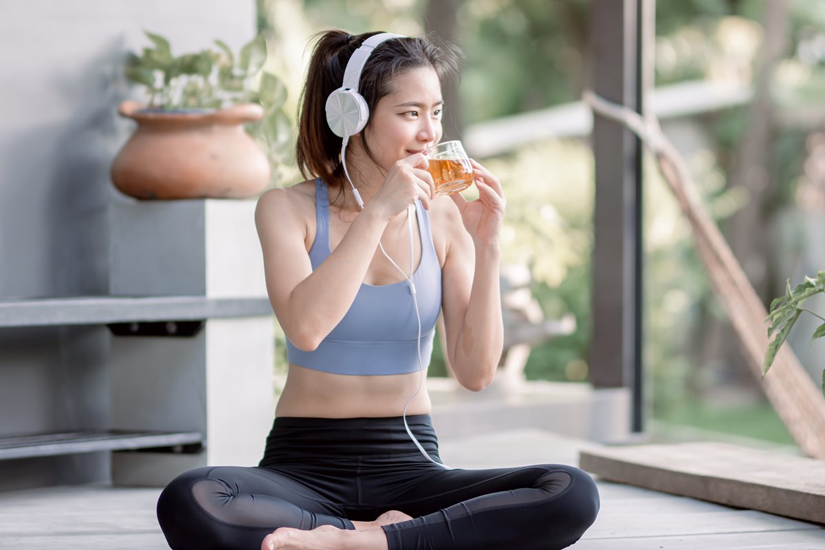 Imagem de uma mulher jovem de roupa de academia tomando chá - Metrópoles