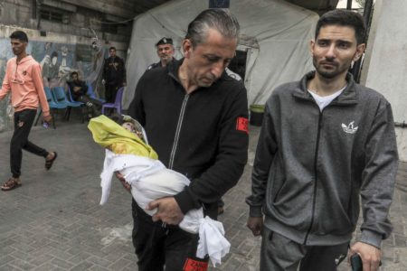 Homem carrega o cadáver de uma criança para enterro no necrotério do Hospital En-Neccar em Rafah, Gaza - metrópoles