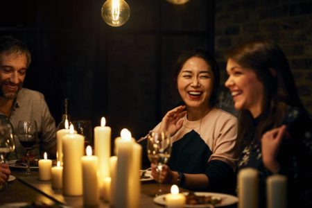 Foto colorida de duas mulheres e um homem sentados à mesa com velas acesas em um jantar - Metrópoles