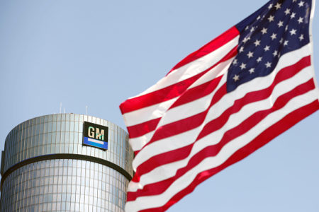 Imagem da bandeira dos Estados Unidos e, ao fundo, uma fábrica da General Motors - Metrópoles