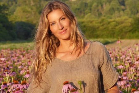 Foto colorida da modelo Gisele Bündchen em campo de flores ao entardecer - Metrópoles