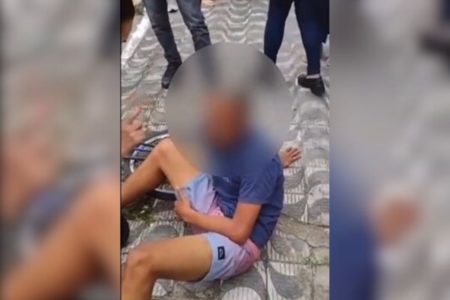 Imagem colorida mostra jovem vestido com uma camiseta azul e bermuda jeans caído no chão ao lado de uma bicicleta; ele roubou o celular de uma idosa na orla de uma praia - Metrópoles