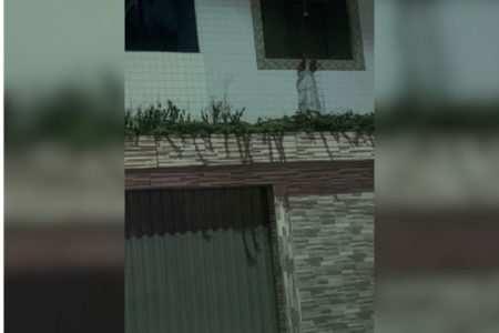 Imagem colorida mostra a fachada de uma casa na Praia Grande, litoral de São Paulo, com um boneco de corpo humano pendurado na janela - Metrópoles