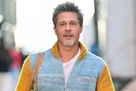 Foto do galã Brad Pitt. Ele é um homem branco, com cabelo grisalho, barba grisalha e um casaco azul com amarelo - Metrópoles