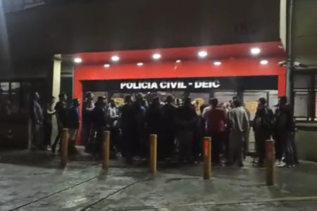 Imagem de porta de delegacia com pessoas reunidas; elas foram vítimas de um golpe feito por pai e filho - Metrópoles