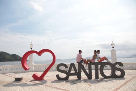 foto colorida de ponto turístico da cidade de Santos, no litoral de SP; turistas sentados sobre escultura com o nome da cidade - Metrópoles