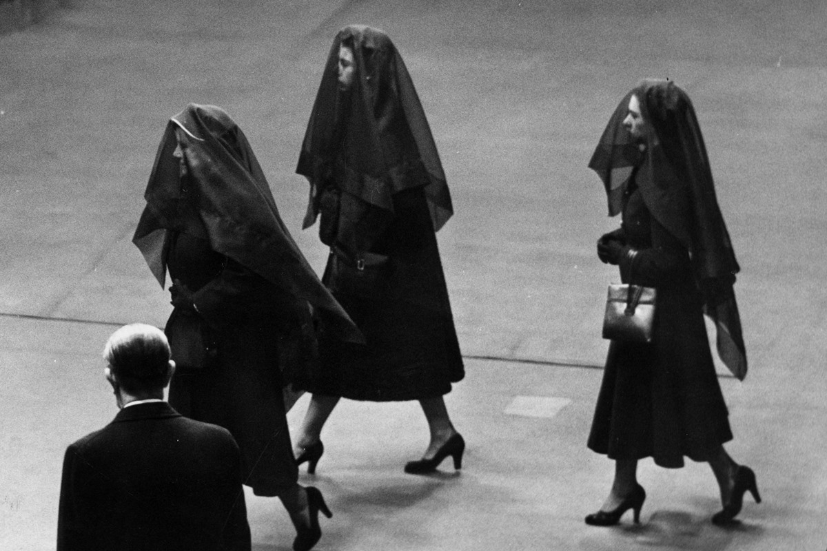 Três mulheres de preto e veus andam em funeral - Metrópoles