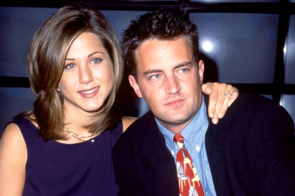 Foto colorida de Matthew Perry e Jennifer Aniston mais novos. Atriz coloca o braço em volta das costas do ator - Metrópoles