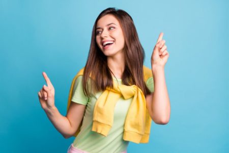 Mulher sorrindo com dedos pra cima de casaco amarelo