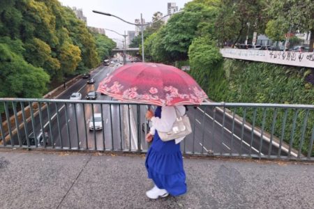 Imagem mostra mulher com guarda-chuva em viaduto - Metrópoles