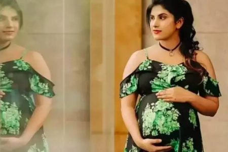 Foto colorida da atriz indiana Priya usando vestido verde e preto e segurando a barriga - Metrópoles