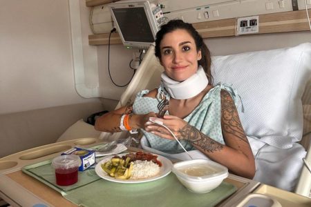 foto colorida de Bianca Andrade sentada em maca de hospital com imobilizador no pescoço e bandeja de comida no colo - metrópoles