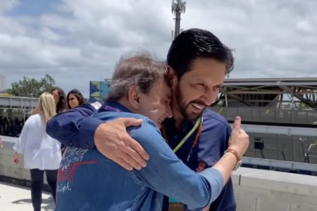 Imagem colorida mostra Ricardo Nunes, homem branco, de cabelo e barba pretos, vestindo camisa azul, abraçando um homem branco, grisalho, de camisa jeans. Eles estão na pista do Autódromo de Interlagos - Metrópoles