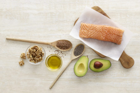 Foto mostra uma mesa com salmão, abacate, azeite de oliva, chia e nozes servidas, alimentos fontes de omega 3 e vitamina F