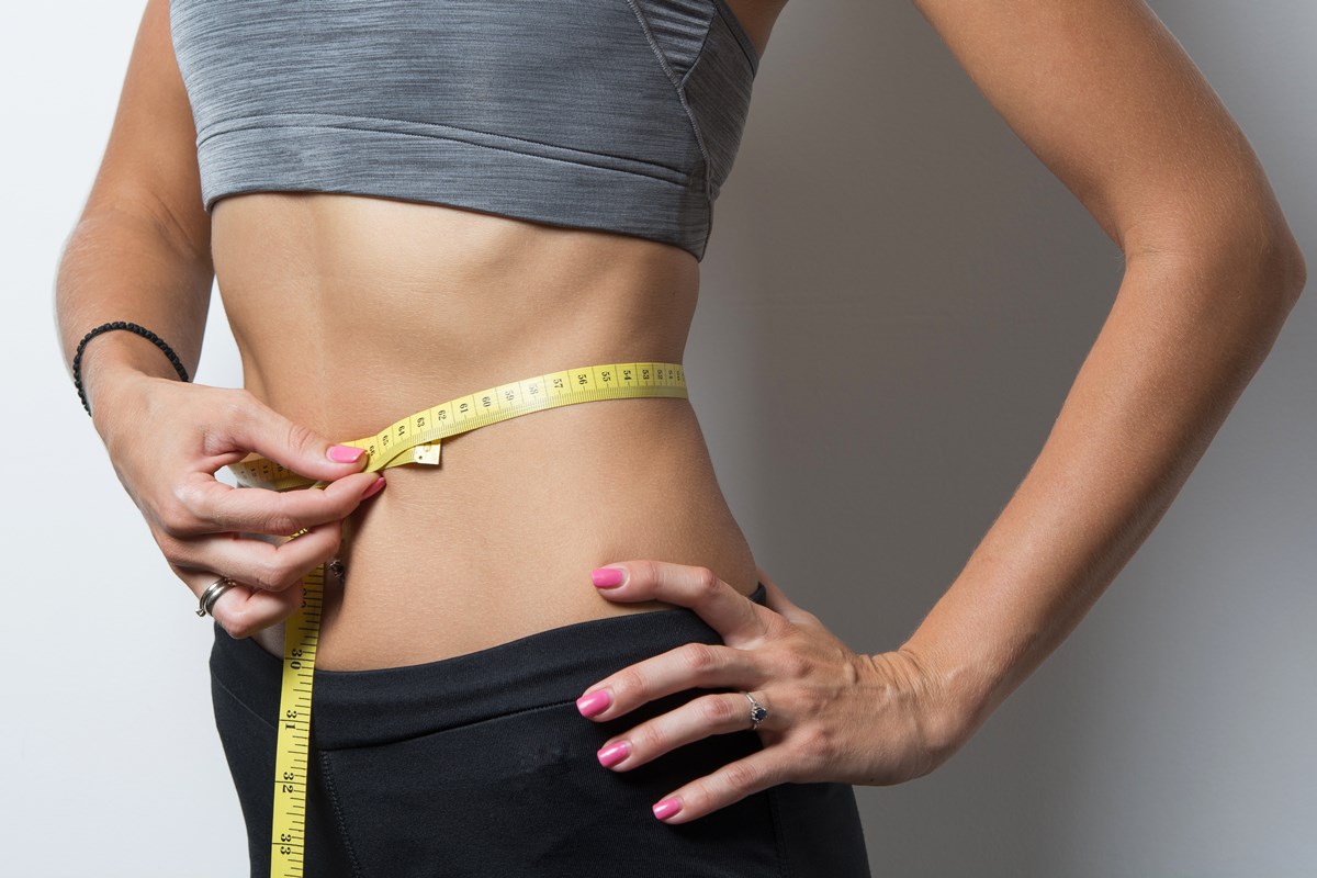 Foto colorida de mulher com fita métrica amarela na barriga e mão na cintura - Metrópoles