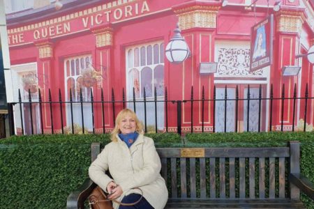 Foto mostra Lesley-Ann Woodhams sentada em um banco público com uma paisagem inglesa ao fundo. Ela preveniu o câncer de mama tomando o remédio anastrasol