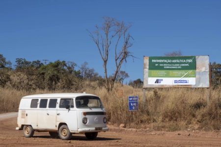 imagem de uma kombi branca andando em uma estrada sem asfalto com uma placa da codevasf ao fundo
