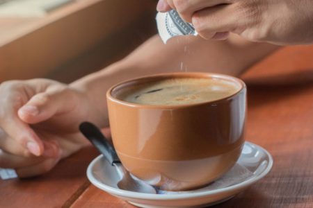 Foto de pessoa colocando açúcar em xícara de café - Metrópoles - cafezinho