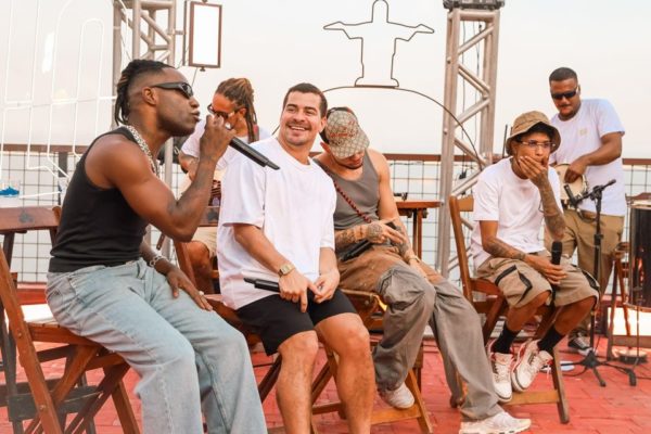 Foto de vários cantores em cima de um palco. Na frente, um homem negro com um microfone - Metrópoles