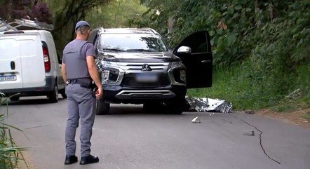 imagem colorida mostra policial em frente à carro em rua de são paulo. ao lado do carro está o corpo de uma pessoa protegido por uma manta térmica - metrópoles