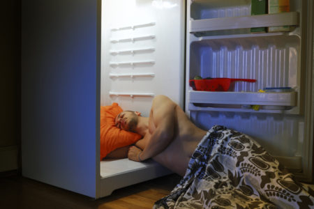 Foto mostra homem deitado dentro de uma geladeira com as portas abertas