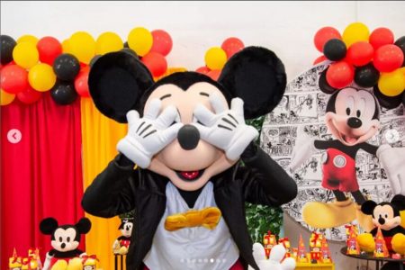 Em foto colorida homem fantasiado de Mickey Mouse cobre os olhos da máscara com ambas as mãos - Metrópoles