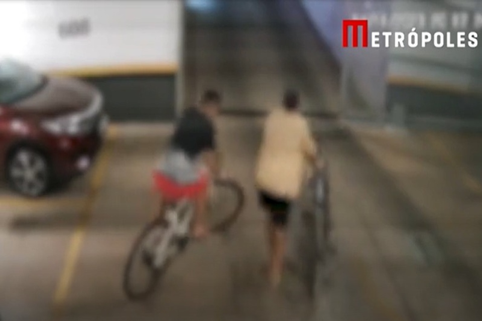 Imagem colorida mostra dois rapazes saindo de garagem com duas bicicletas