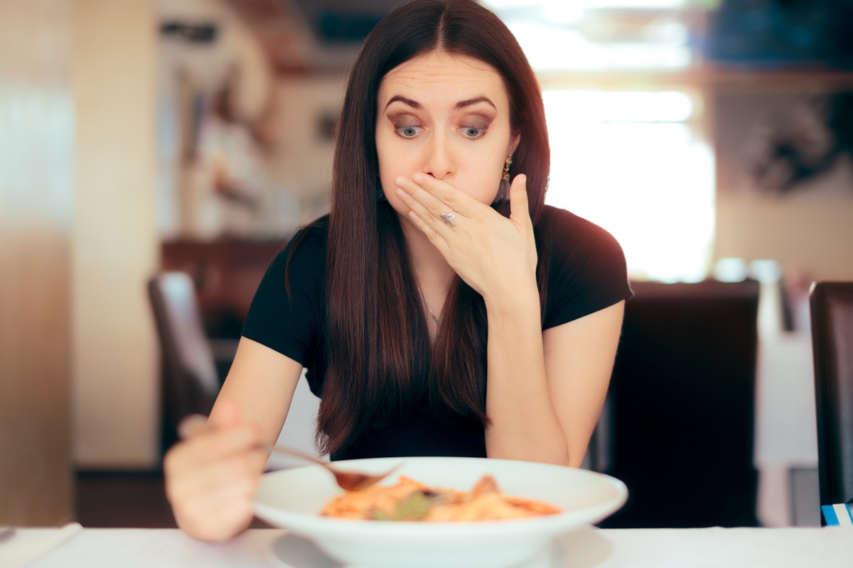 Foto colorida de mulher branca com a mão na boa enquanto olha um prato cheio de comida - Metrópoles