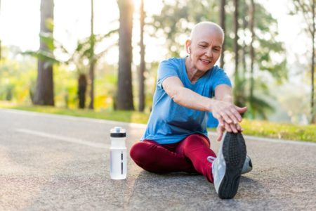 Foto de mulher de cabelo raspado se alongando antes de exercício ao ar livre - Metrópoles