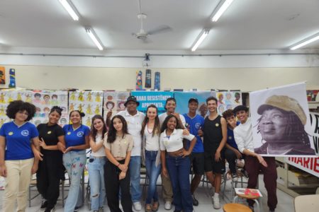 imagem colorida mostra estudantes em escola pública de são paulo. eles estão em uma biblioteca e seguram uma imagem do cantor milton nascimento - metrópoles