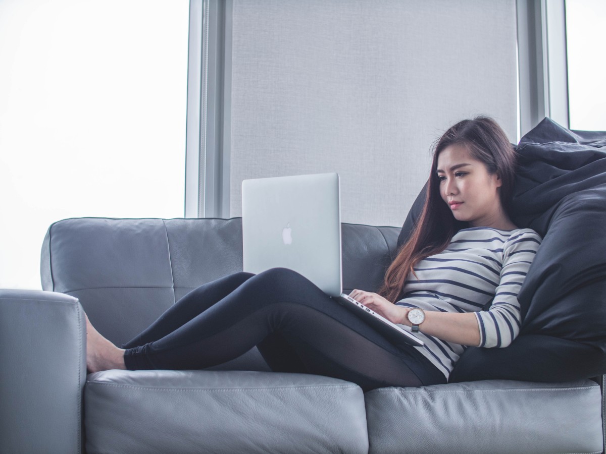 Fotografia colorida mostrando mulher sentada em sofá enquanto usa o macbook-Metrópoles