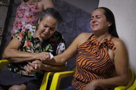 Foto colorida de duas mulheres. No canto esquerdo uma mulher idosa de cabelo branco com roupa florida. No lado direito, uma mulher branca com roupa com estampa de tigre chorando