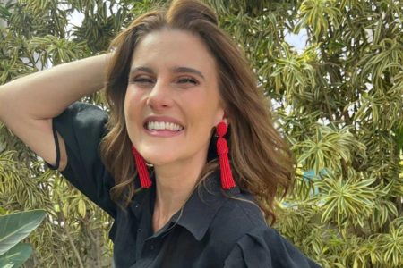 Mulher com cabelos castanho se brinco vermelhos em frente a plantas - Metrópoles