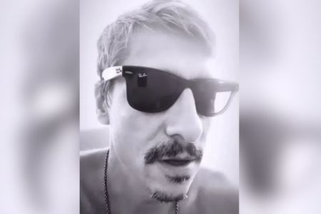 Imagem em preto e branco mostra o cantor Gustavo Fildzz, da banda Aliados, um home branco de cabelo platinado, bigode preto e óculos escuros - Metrópoles