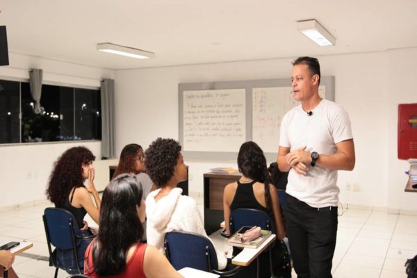 Foto colorida de sala de aula com estudantes e profesor