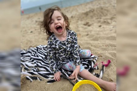 Foto mostra criança brincando em praia. É Imogen, bebê que teve tumor cístico no cérebro - Metrópoles