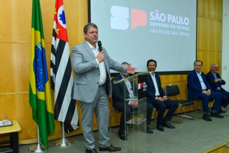 Imagem colorida mostra Tarcísio de Freitas, homem branco, grisalho, de terno cinza e camisa branca, falando em um microfone em um palco - Metrópoles