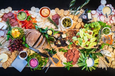 Foto colorida mostra mesa servida com frutas, vegetais e pães dispostos de forma estética