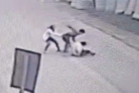Imagem preta e branca de homem socando outro no meio da rua; ele é contido por uma mulher - Metrópoles