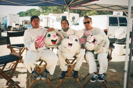 foto colorida de tres homens sentados lado a lado vestidos em fantasias de coelhos - metrópoles