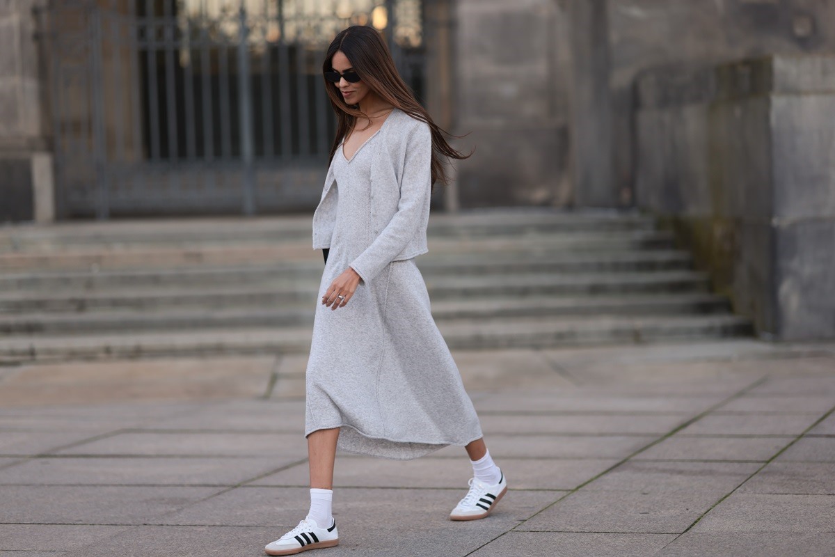 No street style, mulher usa vestido e cardigã cinzas com tênis Samba branco, da Adidas - Metrópoles