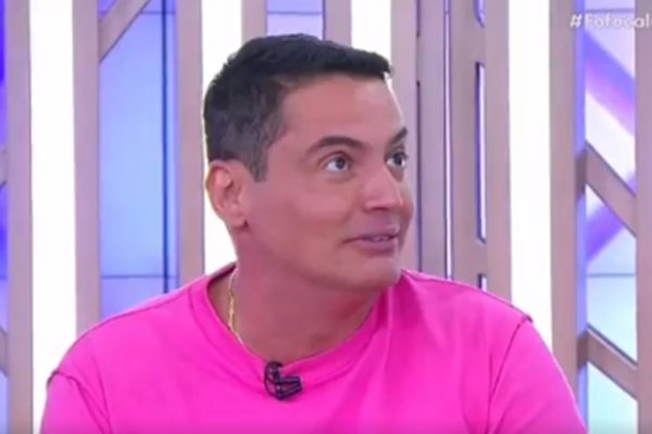 Foto de um homem branco, de cabelo preto, usando blusa rosa - Metrópoles