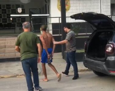 Foto colorida mostra momento em que suspeito de agredir policial é levado à delegacia