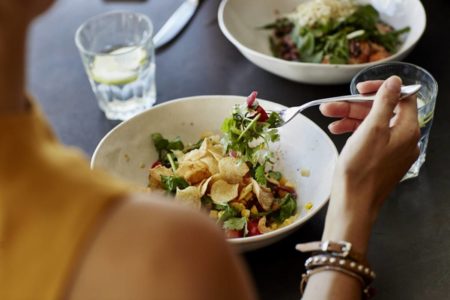 Foto de mulher de costas comando salada com batata crocante - Metrópoles